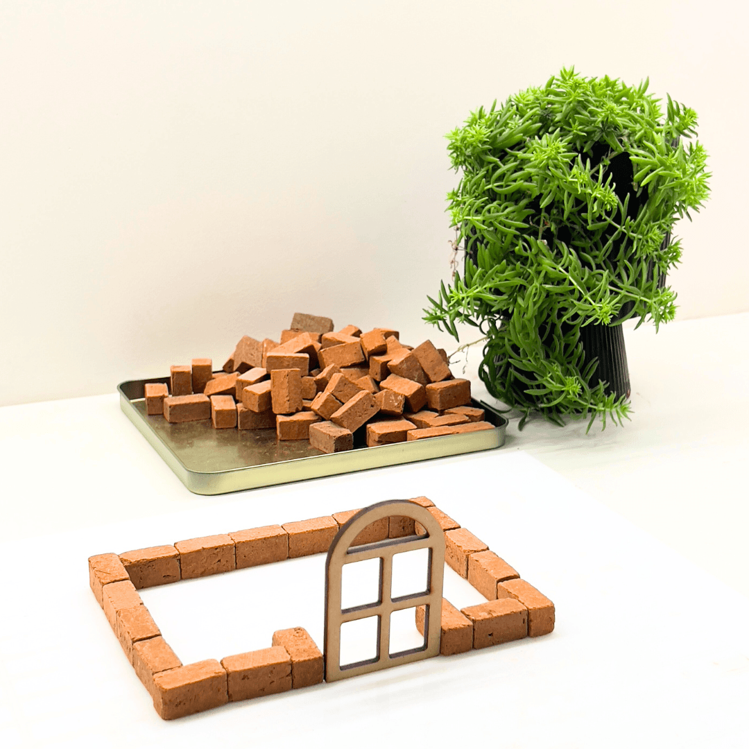 Hands building a miniature model house with real clay bricks
